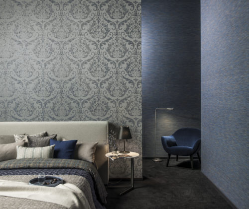 Tactile blue and grey bedroom. Soft pillows in different colours, plaids in different structures. In the corner a blue velvet chair with reading light. Warm carpet on the floor.