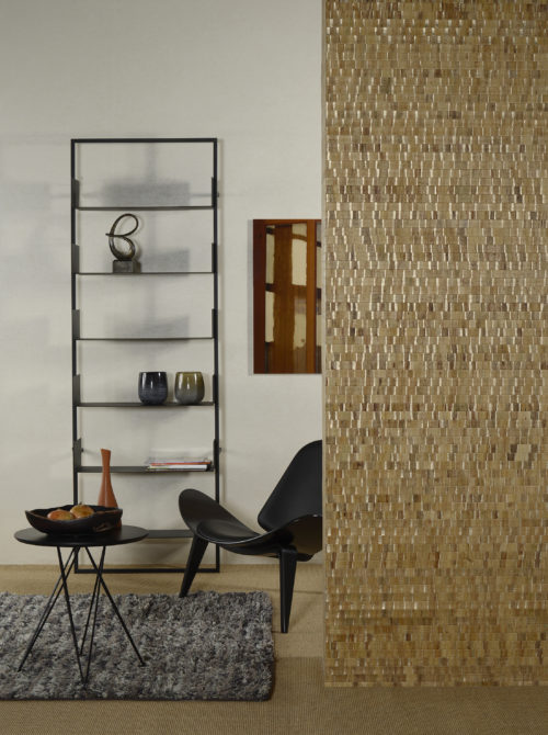 Omexco Nomad: waterlily leaves are woven in lively and generous colours. A detail of the yellow gold in this picture. It is combined with a non-woven wallcovering from the same collection. Black lounge chair and black shelves on the wall.