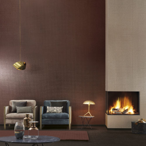 Warm interior picture of a living room with fire place. Two velvet lounge chairs. Impressive folded gold lamp. Two types of mica wallcoverings: one rust, one rosé gold.