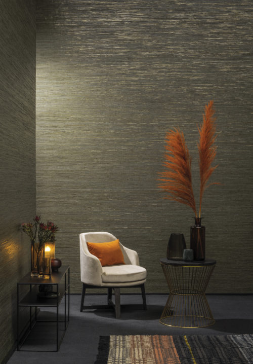 Raffia threads from our Seraya collection: the raffia is delicately coloured in layered pastels or lacquered effects and laminated onto non woven paper. The collage is laid out on a metallic background, evocative of precious minerals. In this picture we see the dark green raffia wallcovering combined with orange details and a cream velvet lounge chair.