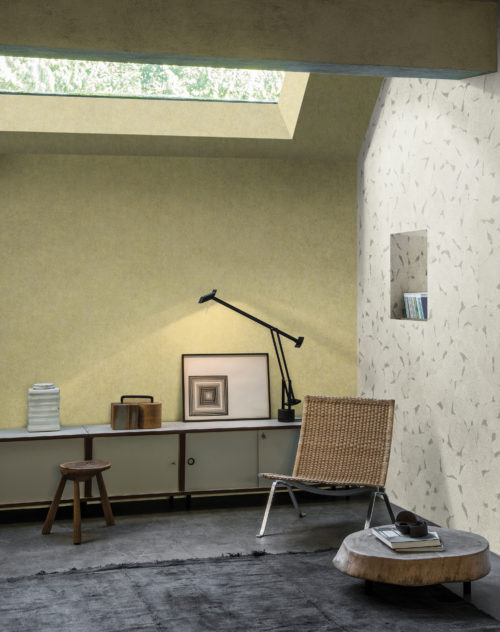 The way the ceiling is shaped, this looks like an attic room. Cosy with rotan lounge chair and console. Soft yellow wallcovering by Omexco.