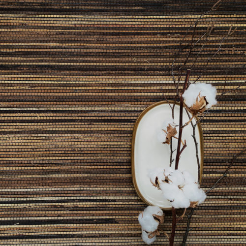 This top shot provides a captivating view of Omexco’s bakbak weave wallcovering from the natural handmade “Intuition” collection. The dynamic wallcovering showcases captivating contrasts and an array of different shades of brown, creating a visually stunning display of texture and depth. Accentuating the wallcovering is a small ceramic white plate adorned with a delicate cotton branch resting on top.