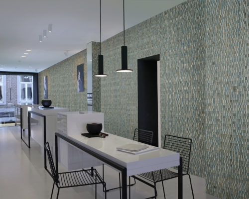 Impressive contemporary show with a white, high white counter. Black wire stools. Black metal lamps, black metal in the door opening. Turquoise stunning waterlily wallcovering from the Omexco Nomad range.