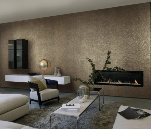 Tactile living room with contemporary fireplace. We see the white leather sofa, black and white consoles on the wall and outstanding golden sfere lamp. The wall is dressed in brown and gold wallcovering by Omexco.