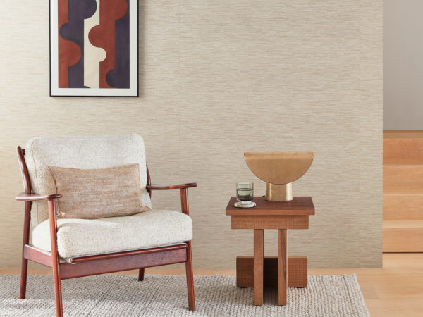 In this image a vintage armchair with a beige cushion is placed on a beige carpet beside a wooden side table with a golden table lamp and a glass of water. On the right a wooden stair with 4 steps. A painting of geometric shapes in navy, white, and rust is hung on the wall on which we see Omexco’s Loom Stories wallcoverings. This elegant linen and cotton weave is shown here in a soothing shades of beige and light brown. The combination of vintage and modern elements adds a touch of elegance and sophistication to this cosy corner.