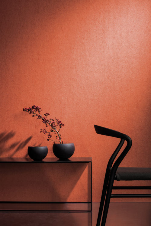 Vibrant orange wallcovering in contrast with a black chair and two dark, round vases on a metal console. Branch with berries.