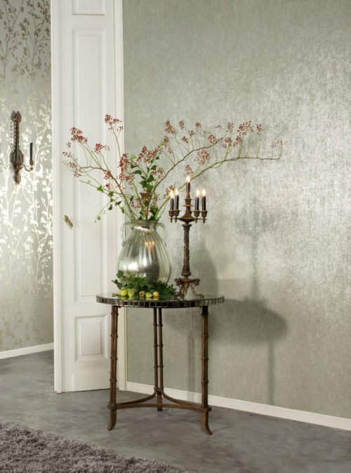 Romantic room showing a silver vase on an antique table. On the wall and on the table are antique chandeliers with dark brown candles. A silver vase brings out the silver in the wallcoverings. Red berry branches.