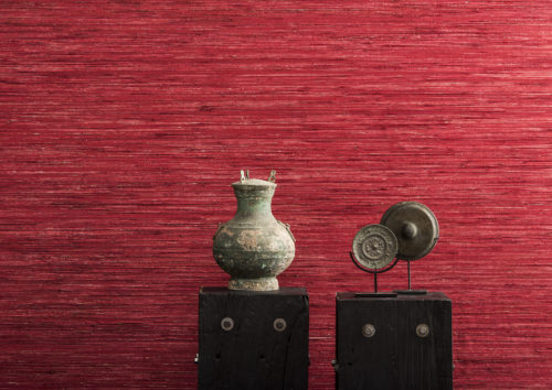 Detail of horizontally installed bright red raffia wallcovering from the Borneo collection. Medieval artworks on pedestals.
