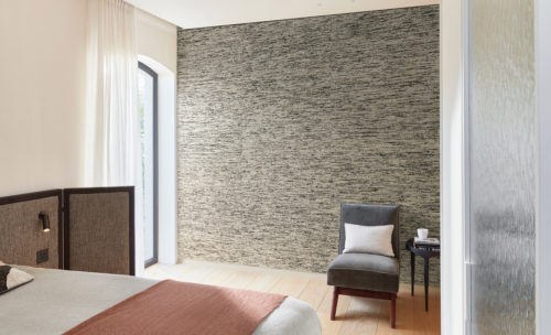 Example of a minimalistic, yet cosy bedroom white a large window on the left, a light oak wooden floor, a double bed with salmon-coloured blanket and a vintage grey single seater. On the wall we see Omexco’s thickly woven textile wallcoverings in off-white and black shades. Woven using the finest natural fibres and expert craftsmanship, each design of Omexco’s "Loom Stories" collection is straight from the handweavers loom to your interior.