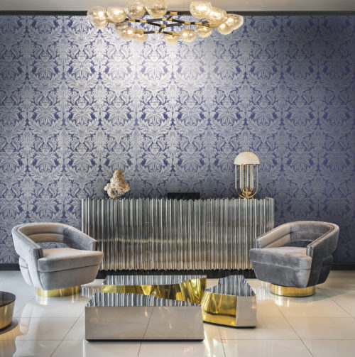 Room with a lot of silver and gold details. Grey velvet chairs, impressive lamps and centre table. The purple damask with silver flowers on the wall goes well with it.