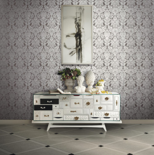Baroque looking room with sideboard full of different drawers. Each drawer has a different handle. On the sideboard a buste and several vases with fruit. On the wall a damask wallcovering with silver foil and an abstract painting.