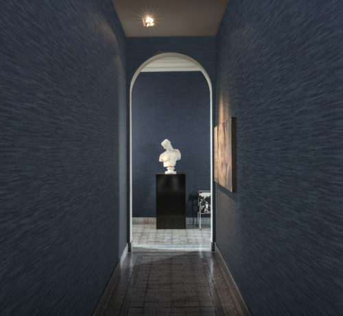 Narrow dark blue hallway looking out on a white buste and a chair with cow's skin. Floor with old tiles.