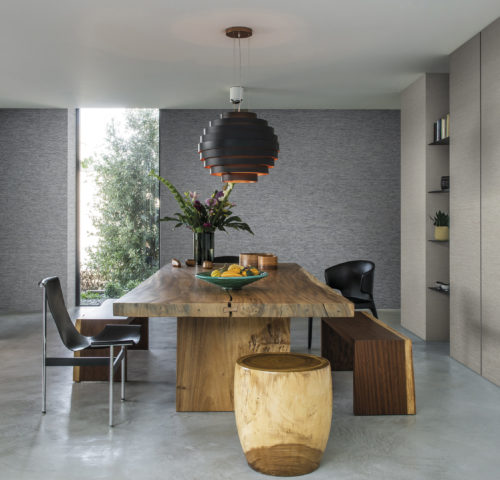 Dining room with wooden table, wooden stool and different black chairs. Concrete floor. Horizontally installed wallcoverings on the walls.
