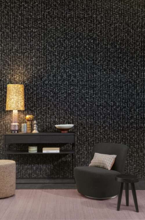 Omexco's tactile tribute to Coco Chanel. The wall of this living room is covered with a chunky weave of black and white handspun yarns, which is an eternal design for timeless modern style. The classy space is styled with two black side tables of different heights,  a lounge chair, beige pouf and carpet of the same colour.
