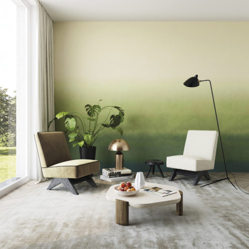 Impressive living room with two single seater sofas, a wooden geometrically shaped coffee table, black minimal floor lamp and large window to bring brightness to the space. We see a feature wall covered with 'Zenitude' design from Omexco's Joy collection: a breathtakingly beautiful gradient with shades of green.