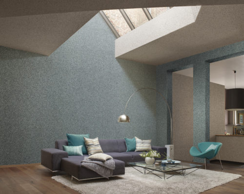 Vast living room with a lot of natural light from a glass piramid in the ceiling. Electric blue mica wallcovering on the wall. Large blue corner sofa with pillows in aqua tones.