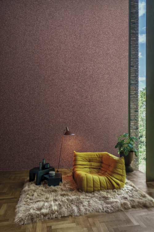 Moonstone by Omexco is a timeless collection of beautiful and oh-so-touchable wallcoverings crafted from natural mica. In this image we see a cosy reading nook with purple textured mica wallcoverings. This is the perfect backdrop for a comfortable single seater sofa in contrasting yellow and beige plush carpet. On the left there is a large window to add brightness to the space. The hardwood floor has an organic design and brings warmth to the space.