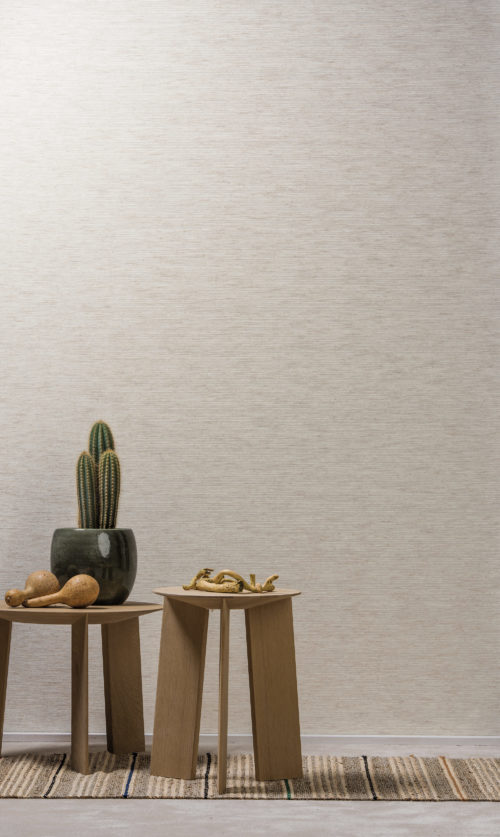 Two wooden stools: one with a cactus and maracas, one with pieces of washed wood. Linen woven wallcovering on the wall.