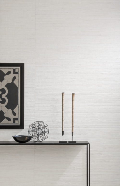 Detail of white wallcovering with jute weave. Black accessories in contrast: artwork, bowl, candles.