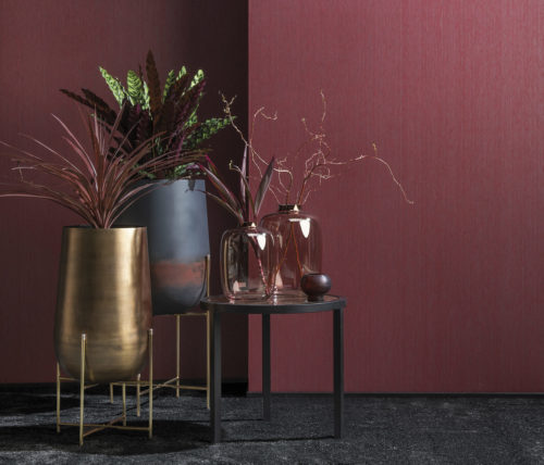 Little group of vases, 3 on an end table with marble top, two on a handcrafted iron statue. Behind it burgundy Portfolio wallcoverings by Omexco.