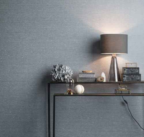 Two console tables in metal. On them light blue and grey accessories. Square glass boxes. Behind it Portfolio wallcoverings. Grey lamp gives a pink hint to the whole.