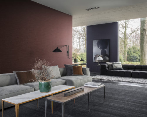 Living room with large windows overlooking a garden with a large tree. Contemporary furniture in grey tones. Green vase with pink blossoms. On the wall Omexco Portfolio wallcoverings in red and blue. On the blue wall a blue picture of a girl with an afro.