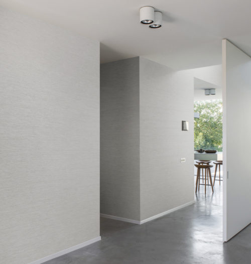 Uniformy coloured living space with high chairs in the back. Omexco Portfolio wallcoverings on all walls.
