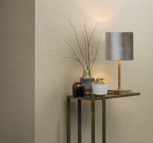 Cream coloured wallcovering, shown horizontally. Metal end table with a gold look. On the table vases with white and grey pearls. Table lamp with metallic shine.