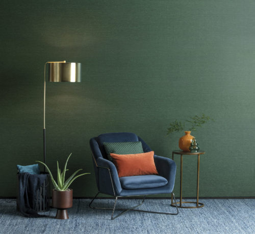 Decor with blue velvet chair, orange and green cushions and vases. Green Portfolio wallcovering on the wall.