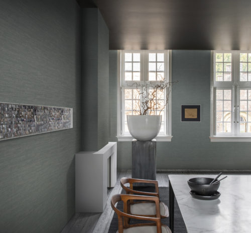 Well lit room with huge white vase and curly branches. On the wall green Omexco wallcoverings and an artwork with recycled pieces of paper.