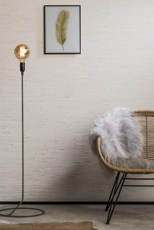 Cosy detail of jute and grass wallcovering on the wall. Chair with fluffy animal skin. Feather artwork on the wall.
