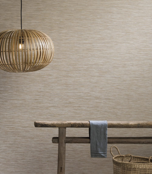 Wall dressed with Omexco Portfolio wallcovering, antique wooden side table, rotan lamp, basket.