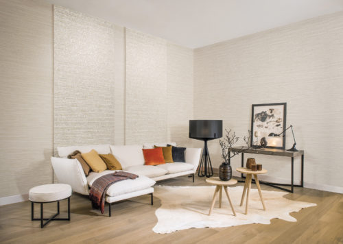 Living room with white sofa with thick cushions. Pillows in earth tones. Grand black standing lamp. Shades of Pale and Capiz wallcoverings on the wall.