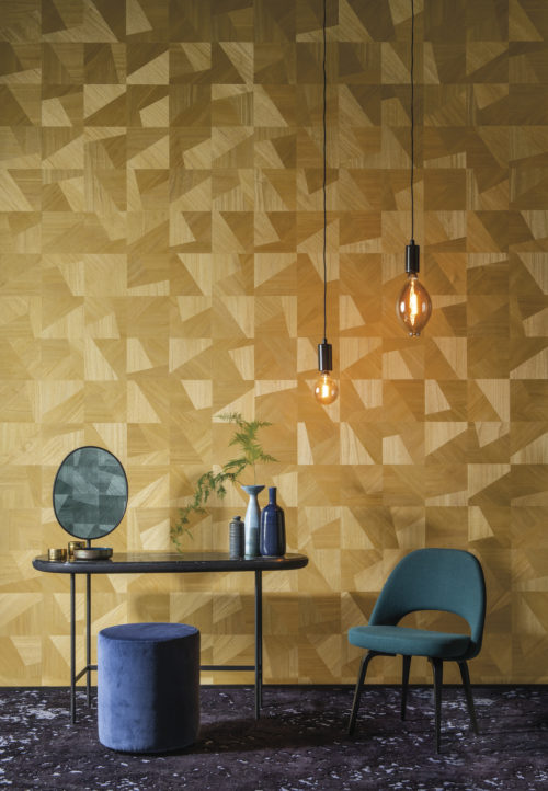 In this picture an example of how the Omexco Sycamore collection embodies natural beauty and soft glamour. A beautiful contrast between the yellow dimensions design of chic interlocking wood textures with green interior details: a chair, pouf, pendulum lights and in the mirror we see the same wallcovering in green appear.