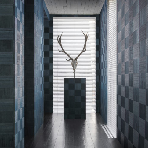 The Sycamore collection by Omexco is uniquely defined by a celebration of natural wood.  Our elegant and refined wallcoverings bring to life this noble and authentic material. We see a well lit hallway presenting the blue 'chess' design: squares of wood in different direction like a chess board.