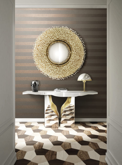 Picture of a chrome console that reflects the wooden inlay floor. Above it a round mirror with mother-of-pearl dots. Behind it horizontally installed Infinity striped wallcovering.