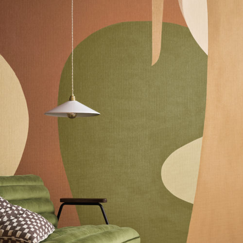 This vibrant interior showcases Omexco’s OAS211 reference, Alegre, from the Oase collection. The panoramic wallcovering, inspired by naïve art, features an abstract composition of organic shapes in earthy tones, evoking the sweeping landscapes of South America. The interplay of warm terracotta, olive green, and beige hues brings depth and movement to the space. A plush green velvet sofa harmonizes with the design, while a geometric-patterned cushion and a minimalist pendant light enhance the room’s refined yet cozy ambiance. The overall setting exudes a balance between artistic expression and sophisticated comfort.