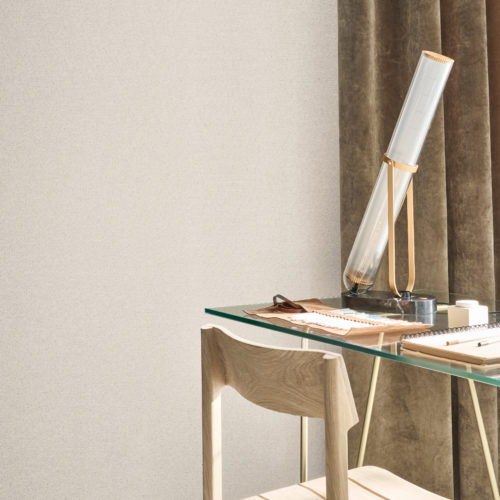 This serene workspace captures the understated elegance of Omexco's Pure collection, reference PU202, titled Resource. The wallpaper showcases a refined weave of twisted paper, artfully blending two different yarns of varying thicknesses and shades. The soft, textured surface subtly reflects the light, adding depth and warmth to the space. A modern glass desk paired with a minimalist wooden chair complements the neutral tones of the wallpaper, while a contemporary lamp with brass accents adds a touch of sophistication. The rich velvet curtains in earthy hues complete the setting, creating a tranquil and inspiring environment.