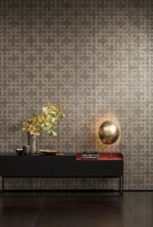 Low table with vase with oak branches, golden ball lamp, cork wallcovering with geometric design in the back.