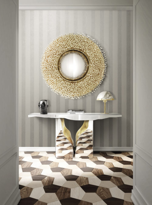 Picture of a chrome console that reflects the wooden inlay floor. Above it a round mirror with mother-of-pearl dots. Behind it horizontally installed Infinity striped wallcovering.