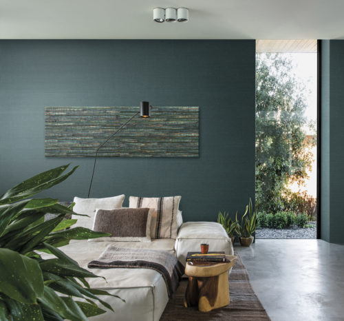 Green interior of a bedroom with concrete floor. Bed with assorted pillows, close to the floor. Aruba wallcovering on the wall. On the wall an artwork of the waterlily from the same wallcovering collection.