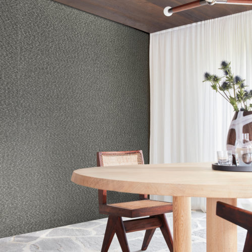 Image of a bright dining room with floor-to-ceiling white sheer curtains, a natural stone floor, a minimalist Scandinavian-style dining table with matching chairs and textured black and white Omexco wallcoverings. This linen bouclé yarn from the Loom Stories collection appears as stimulating to the eye as it does to the touch. The room is well-lit and spacious, with ample natural light streaming in through the windows. The simple yet elegant decor elements create a cozy and inviting atmosphere.