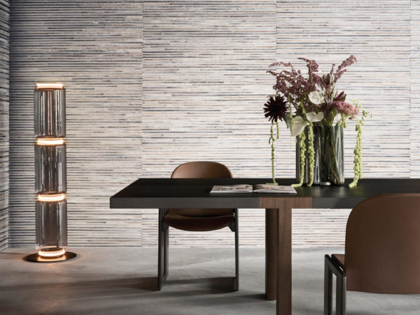 This refined interior showcases Omexco’s LAN211 reference, Moonlight, from the Light at Night collection. The wallcovering, woven from abaca fibers, features contrasting metallic threads that create a delicate interplay of texture and sheen. The soft, natural tones blend seamlessly with the minimalist design of the room, where a dark wood dining table and leather chairs introduce warmth and sophistication. A sculptural floral arrangement in glass vases adds an organic touch, enhancing the harmony between nature and craftsmanship in this elegant setting.