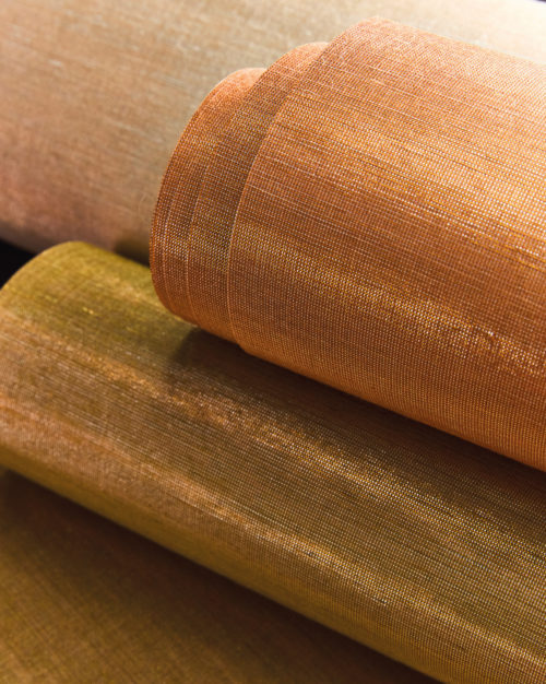 A selection of wallcovering rolls from the LAN collection, showcasing the rich textures and shimmering hues of silk. The image features LAN231, LAN232, and LAN233, each revealing the natural elegance of silk with radiant golden and copper tones. The interplay of light enhances the luxurious sheen, emphasizing the depth and refinement of the material.