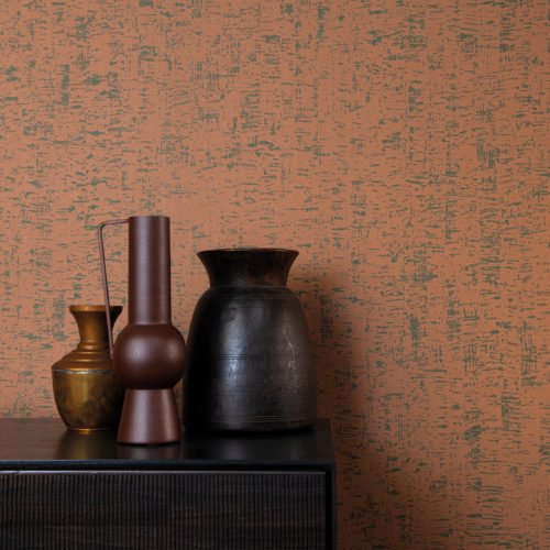 The High Performance Patina Wallcovering collection by Omexco combines performance with sustainability and modern aesthetics. This image shows an interesting printed non-woven wallcovering in burnt orange. The perfect backdrop for a dark brown wooden cupboard on which three metal vases in earth tones are posed. The wallcovering design,“ Clay”, is inspired by the clay walls and an old painting technique in which thin lime plaster is spread on the wall.