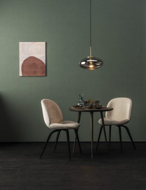 In this picture, we see a small dining table with two white chairs and a glass pendulum lamp. On the walls, Omexco's High Performance Texture wallcoverings are shown. We see the design 'linen' in moss green. It's the design that reminds us most of the local knowhow of working with Belgian linen.