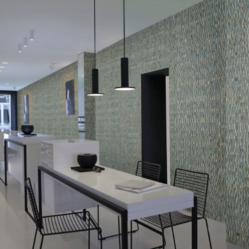 Impressive contemporary show with a white, high white counter. Black wire stools. Black metal lamps, black metal in the door opening. Turquoise stunning waterlily wallcovering from the Omexco Nomad range.