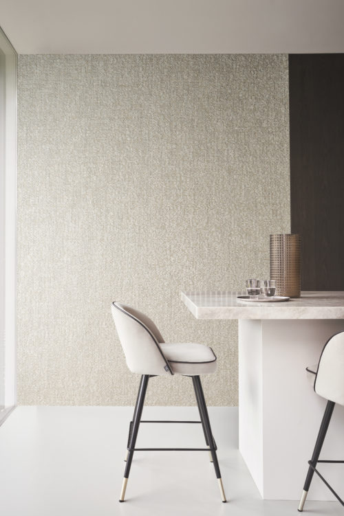 A stylish kitchen featuring a luxurious marble countertop adorned with two soft, comfortable barstools. In the background, Omexco's capiz mother of pearl wallcoverings from the Archipelago collection create an elegant backdrop. The shimmering shades of beige in the textured wallcoverings add a touch of sophistication and refinement to the kitchen space