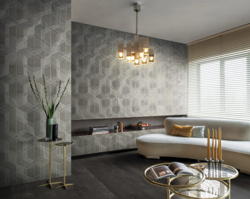 On the walls of this living room: the cubist design in taupe from Omexco's Sycamore collection. It's a wood veneer wallcovering with a geometrical interlocked pattern. The wallcovering is paired with a beige sofa, golden retro glass lamp, yellow pillow, yellow candles and golden side tables.
