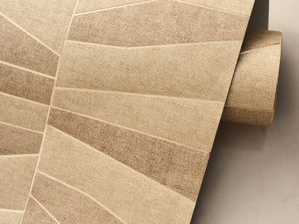 A close-up of an unrolled wallpaper roll from the Oase collection, featuring the OAS231 reference, Domino. This design showcases a patchwork of paperweave, meticulously crafted from geometric shapes that create a dynamic visual effect. The structured pattern rests upon a metallic backing, available in gold or silver, adding a subtle shimmer and depth to the texture. The neutral, earthy tones highlight the natural beauty of the material, enhancing the organic aesthetic of the composition.